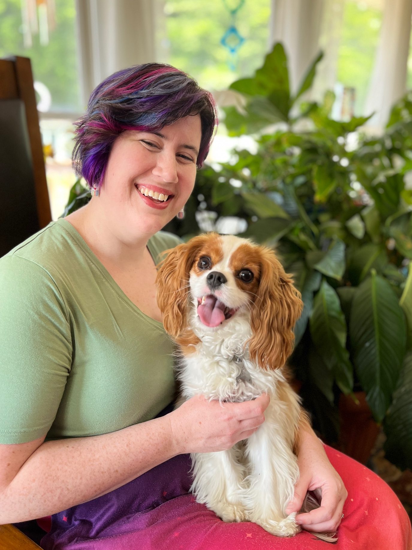 Colleen sits holding a small, red and white Cavalier King Charles Spaniel on her lap