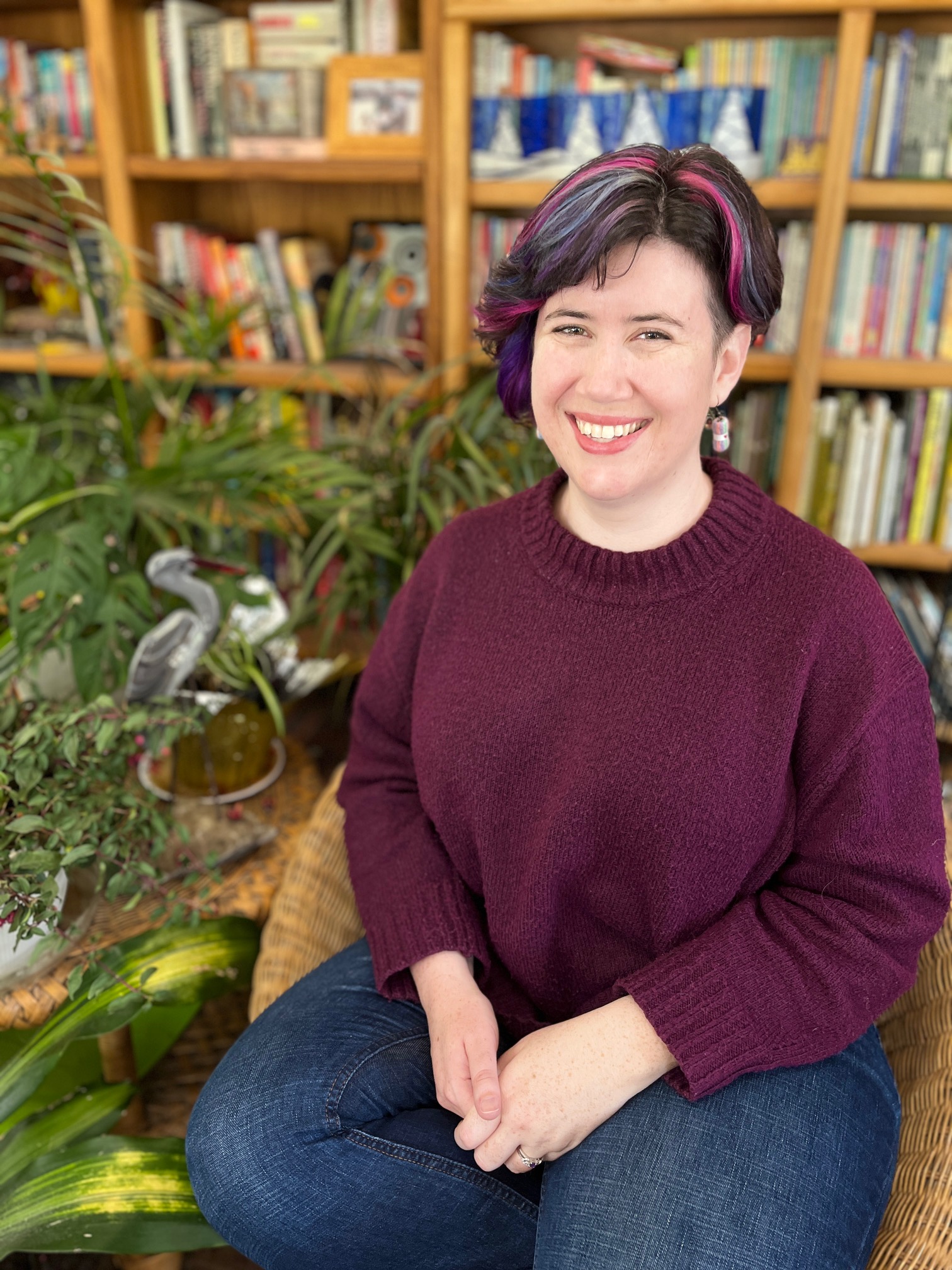 Colleen, a white woman with multicolored hair, sits smiling at the camera